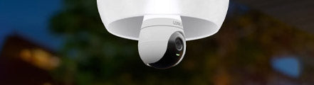 Lorex 2K Wi-Fi lightbulb security camera mounted in an outdoor ceiling fixture at dusk, with its status light glowing and surroundings softly lit.