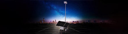 A solar-powered security camera trailer system in an empty lot at night, with a city skyline in the background. The trailer features large solar panels and a tall, extendable pole with multiple security cameras for remote surveillance.