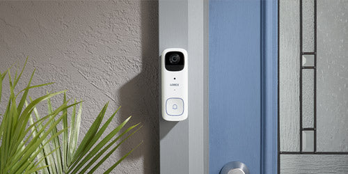 Lorex 2K battery-powered video doorbell mounted next to a front door, shown in a modern residential entryway setting.