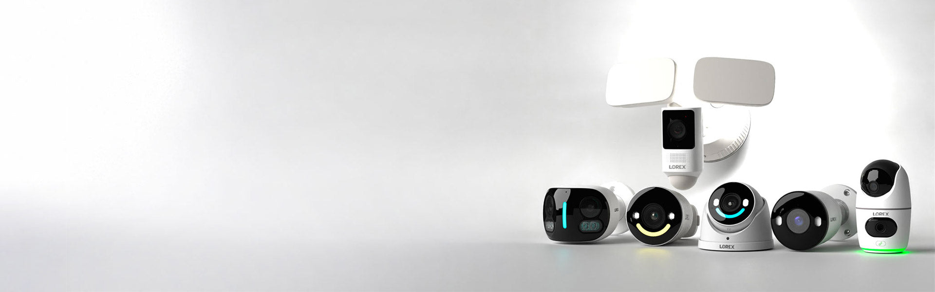 A lineup of Lorex security cameras displayed on a light gray background, featuring various models including IP cameras, Wi-Fi (wireless) cameras, a floodlight camera, a dual-lens camera, and others with sleek modern designs. Some cameras have glowing LED indicators and a mix of black and white finishes, highlighting versatility in home and business surveillance options.