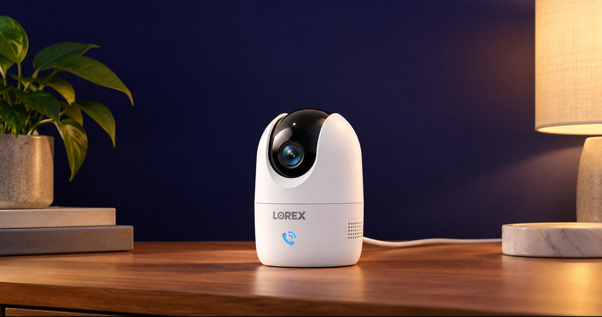 Lorex Connect 2K Wi-Fi indoor pan-tilt security camera displayed on a wooden table beside a lamp and houseplant.