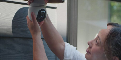Woman installing a Lorex 2K Wi-Fi lightbulb security camera into an outdoor light socket on a home exterior, showcasing simple DIY setup for home surveillance.